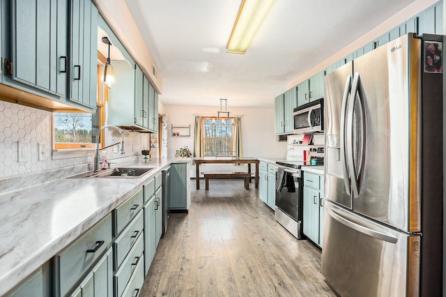 kitchen with sink, hanging light fixtures, light hardwood / wood-style flooring, appliances with stainless steel finishes, and tasteful backsplash