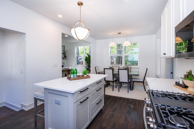 kitchen featuring pendant lighting, dark wood-type flooring, stainless steel gas range, a kitchen island, and a kitchen bar