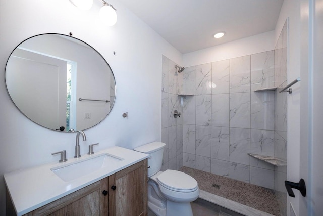 bathroom with a tile shower, vanity, and toilet