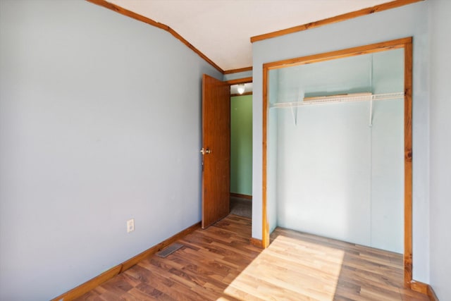 unfurnished bedroom with hardwood / wood-style flooring, vaulted ceiling, a closet, and crown molding