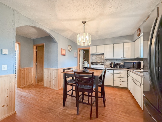 dining area with a chandelier, wood walls, light hardwood / wood-style floors, and a textured ceiling