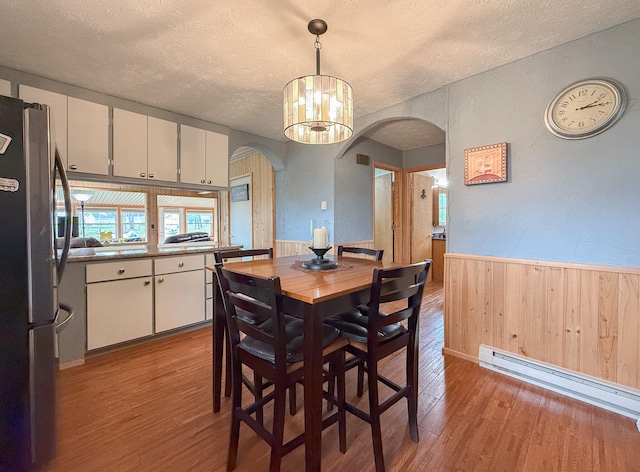 dining area featuring light hardwood / wood-style flooring, wooden walls, baseboard heating, a textured ceiling, and an inviting chandelier