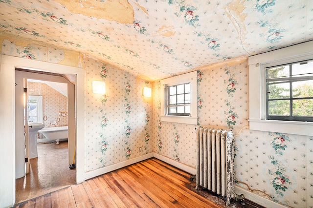 empty room featuring hardwood / wood-style floors, radiator heating unit, and vaulted ceiling