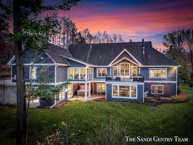 back house at dusk featuring a lawn and a balcony