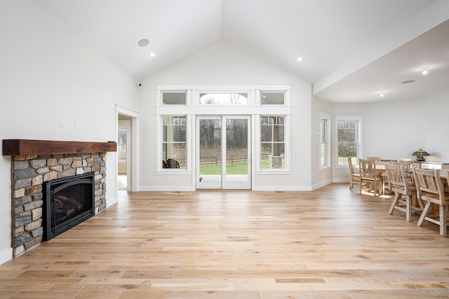 living room featuring light hardwood / wood-style floors, a stone fireplace, and high vaulted ceiling