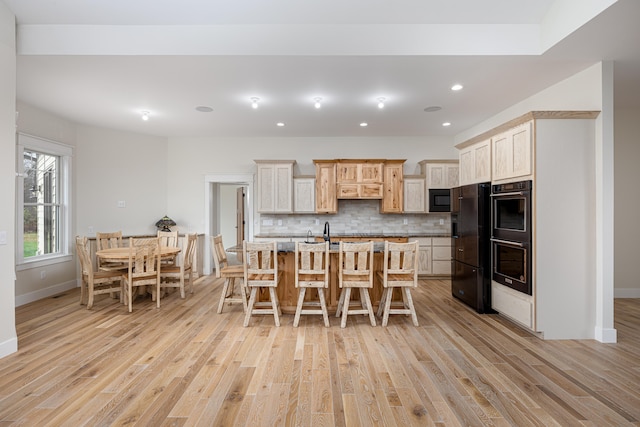 kitchen featuring decorative backsplash, double wall oven, black microwave, a center island with sink, and a breakfast bar area