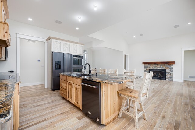 kitchen featuring sink, a stone fireplace, an island with sink, a breakfast bar, and black appliances