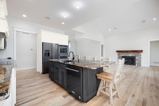 kitchen with sink, dark stone countertops, a breakfast bar area, a fireplace, and black appliances