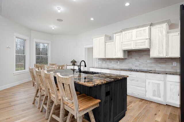 kitchen featuring a center island with sink, a kitchen breakfast bar, white cabinetry, and dark stone counters