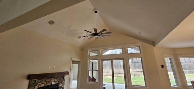 interior space with a stone fireplace, ceiling fan, a healthy amount of sunlight, and lofted ceiling