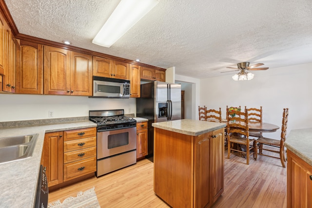 kitchen with appliances with stainless steel finishes, light wood-type flooring, a textured ceiling, ceiling fan, and a center island