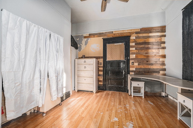 interior space with ceiling fan, built in desk, wood-type flooring, and wooden walls