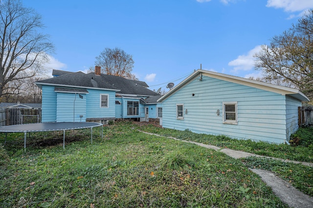 rear view of property featuring a lawn and a trampoline