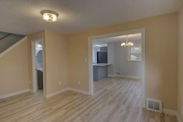 unfurnished living room with light wood-type flooring, a textured ceiling, and an inviting chandelier