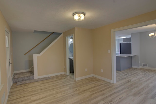 unfurnished living room featuring light hardwood / wood-style floors, a textured ceiling, and an inviting chandelier