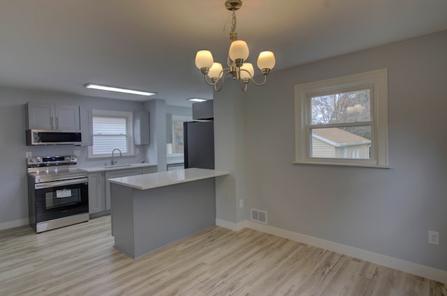 kitchen with stainless steel appliances, an inviting chandelier, light wood-type flooring, gray cabinetry, and pendant lighting