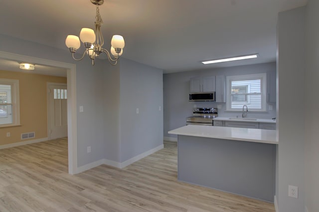 kitchen with appliances with stainless steel finishes, light hardwood / wood-style floors, decorative light fixtures, and sink