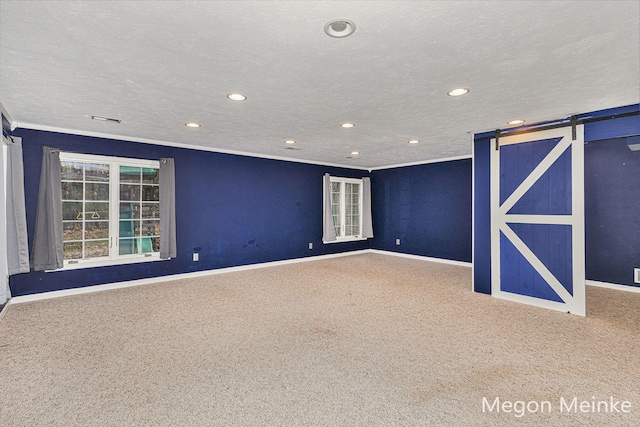 unfurnished room featuring a barn door, a textured ceiling, carpet floors, and ornamental molding