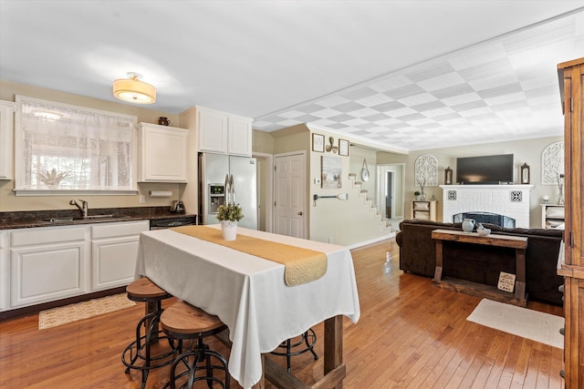 kitchen with white cabinets, stainless steel fridge with ice dispenser, sink, and light hardwood / wood-style flooring