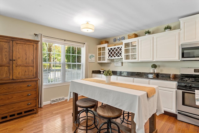 kitchen featuring a kitchen breakfast bar, white cabinetry, stainless steel appliances, and light hardwood / wood-style floors