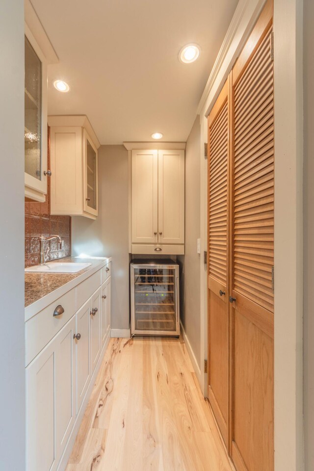 kitchen featuring white cabinets, wine cooler, sink, backsplash, and light hardwood / wood-style flooring