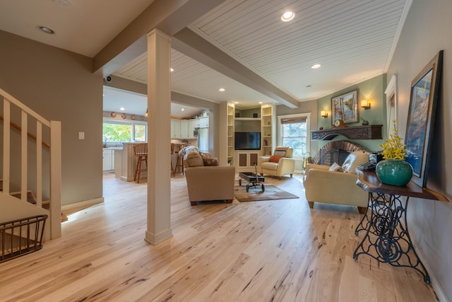 living room with beamed ceiling, wood ceiling, a brick fireplace, built in shelves, and light hardwood / wood-style flooring