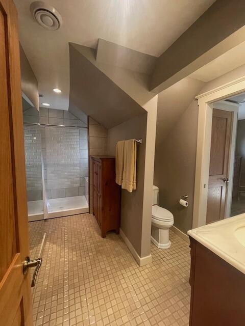 bathroom with a tile shower, toilet, vaulted ceiling, and vanity