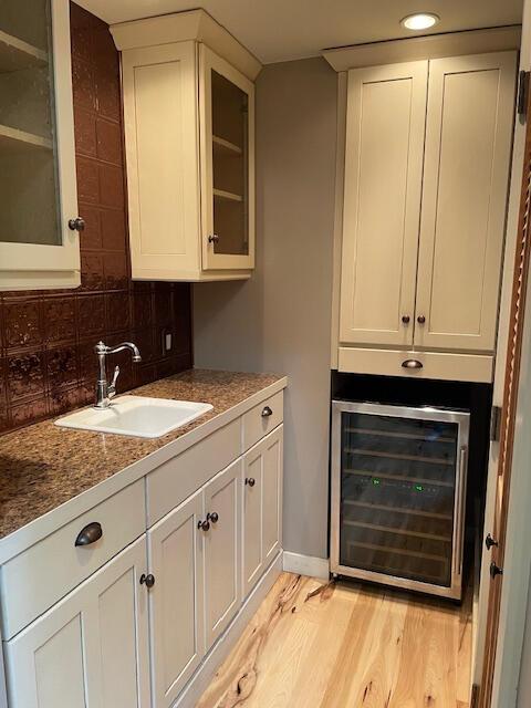 bar with light hardwood / wood-style flooring, sink, white cabinets, tasteful backsplash, and beverage cooler