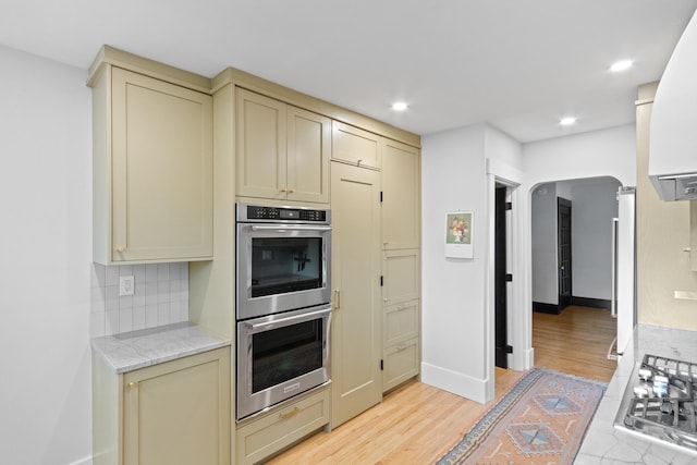 kitchen featuring backsplash, light stone counters, stainless steel appliances, cream cabinetry, and light hardwood / wood-style floors