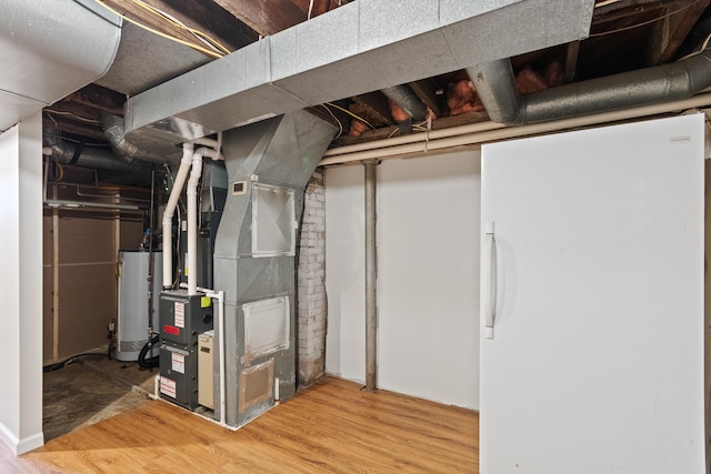 basement featuring heating unit, white fridge, wood-type flooring, and gas water heater