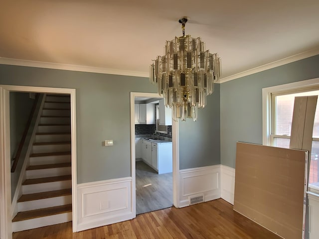 unfurnished dining area featuring hardwood / wood-style flooring, ornamental molding, sink, and a chandelier