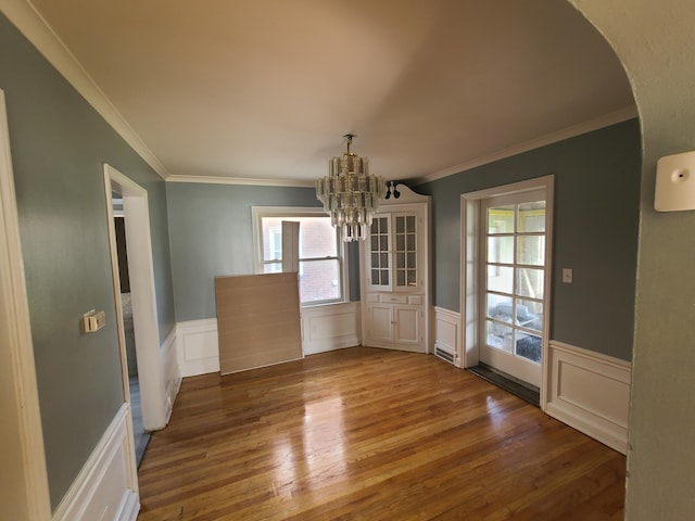 unfurnished dining area with wood-type flooring, an inviting chandelier, and ornamental molding