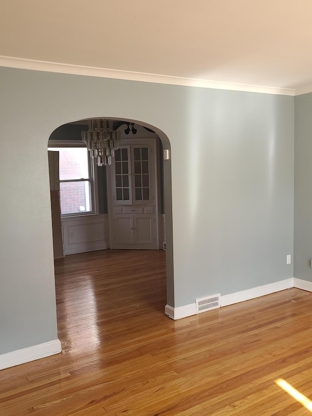 unfurnished room with hardwood / wood-style flooring, an inviting chandelier, and ornamental molding