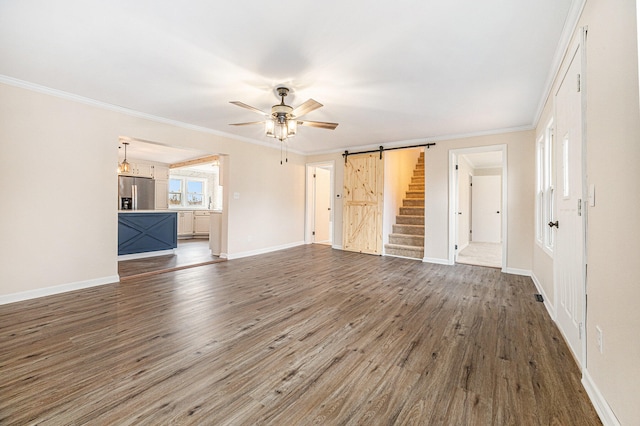 unfurnished living room featuring ornamental molding, ceiling fan, a barn door, and dark hardwood / wood-style floors