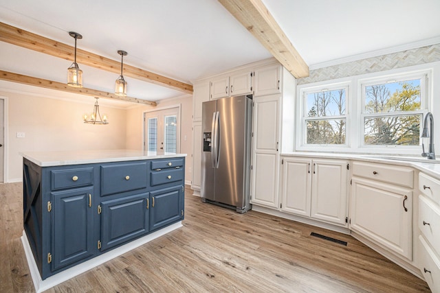 kitchen with blue cabinets, light countertops, stainless steel fridge, and white cabinetry