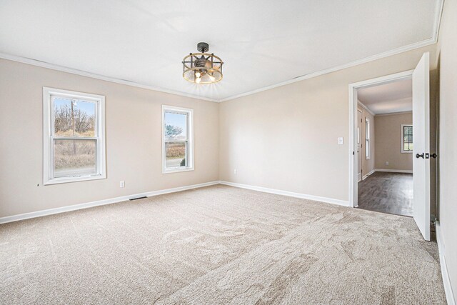 carpeted spare room featuring a healthy amount of sunlight, crown molding, visible vents, and baseboards