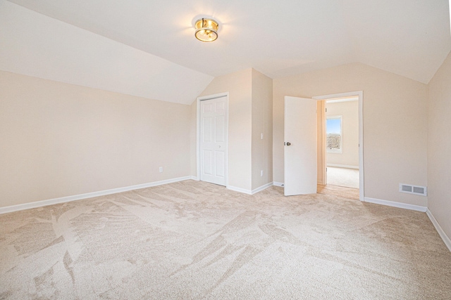 unfurnished bedroom with baseboards, visible vents, vaulted ceiling, and light colored carpet