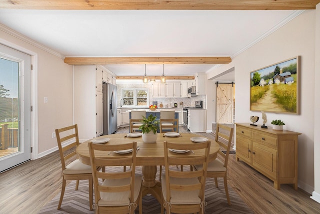 dining space with beam ceiling, crown molding, light wood-style flooring, a barn door, and baseboards