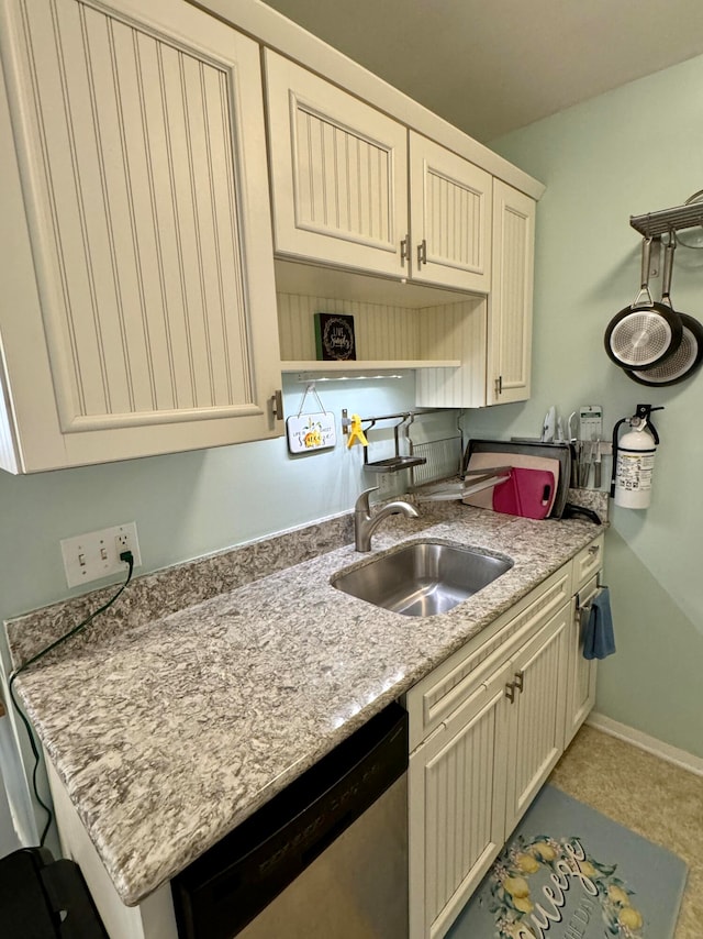 kitchen with light stone countertops, cream cabinets, stainless steel dishwasher, and sink