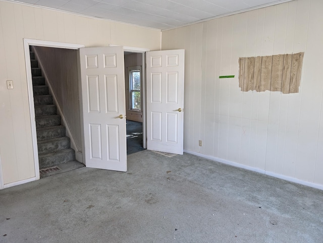 empty room with ornamental molding, wooden walls, and light carpet