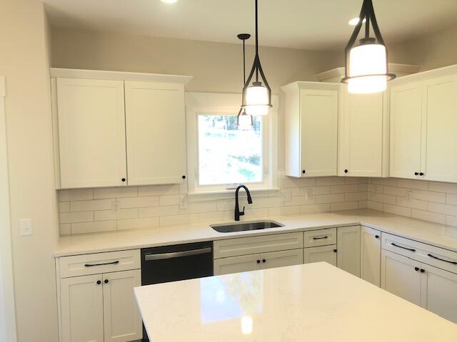 kitchen with decorative backsplash, sink, white cabinets, black dishwasher, and hanging light fixtures