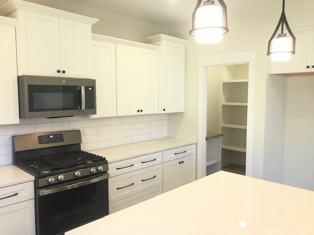 kitchen featuring decorative light fixtures, decorative backsplash, white cabinetry, and stainless steel appliances