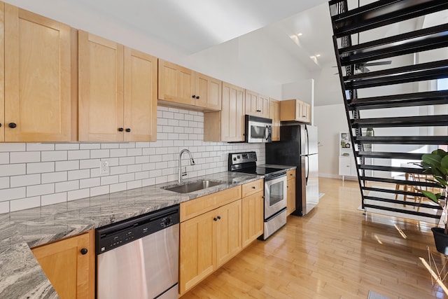 kitchen featuring sink, light stone counters, appliances with stainless steel finishes, light brown cabinets, and light hardwood / wood-style flooring