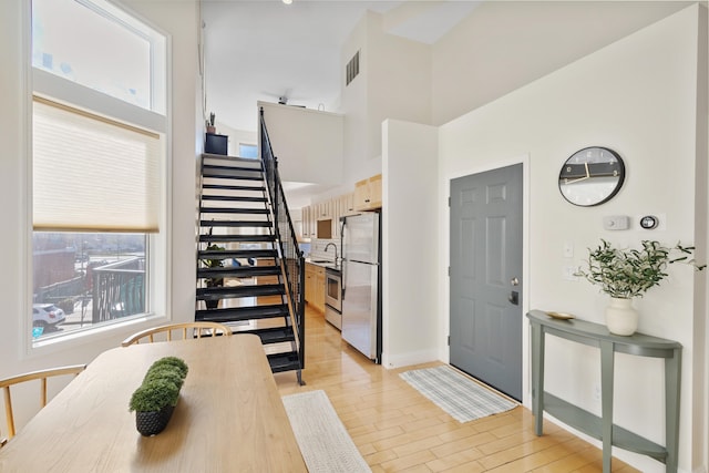 entryway with a towering ceiling, sink, and light wood-type flooring