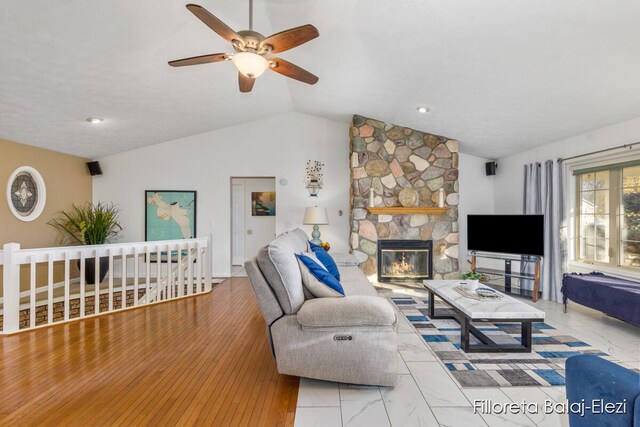 living room featuring vaulted ceiling, ceiling fan, wood-type flooring, and a stone fireplace