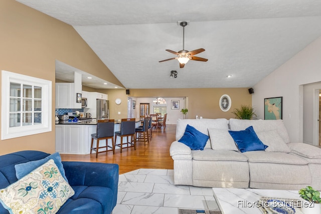 living room featuring light hardwood / wood-style flooring, vaulted ceiling, ceiling fan with notable chandelier, and a textured ceiling