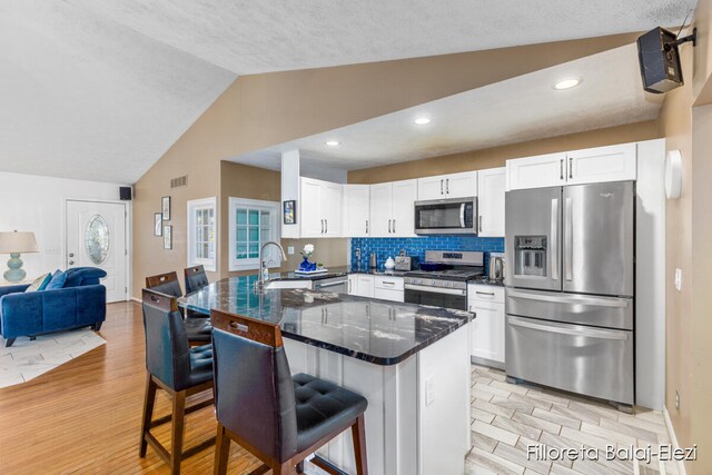 kitchen with light hardwood / wood-style floors, vaulted ceiling, a breakfast bar area, white cabinets, and appliances with stainless steel finishes