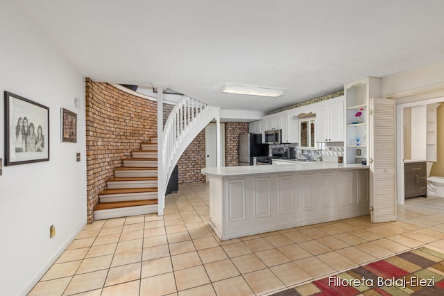 kitchen with white cabinetry, stainless steel appliances, brick wall, kitchen peninsula, and light tile patterned floors