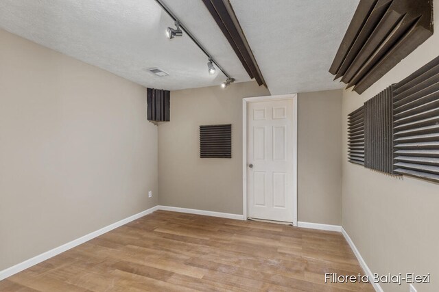 basement featuring a textured ceiling, light wood-type flooring, and rail lighting