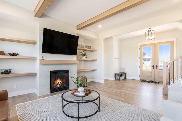 living room with french doors, a tile fireplace, light hardwood / wood-style floors, and beam ceiling